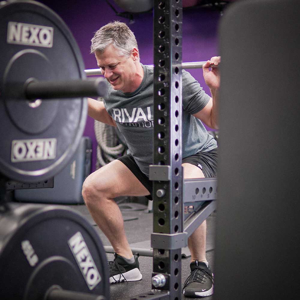 Professional strength training at Galaxy Fit Lab Bonita Springs - client performing barbell squat with proper form in high-end gym facility with NEXO equipment